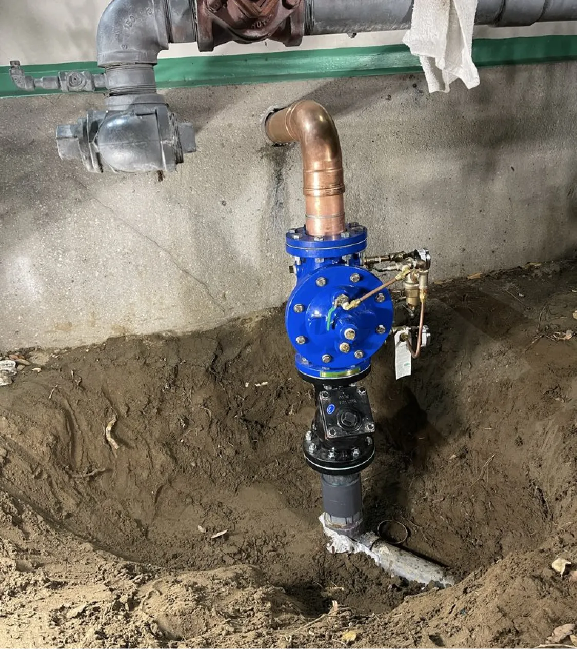 A blue industrial valve assembly is installed in a dirt trench with pipes attached above and below.