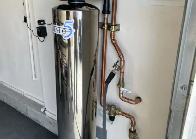 A water softener system with copper pipes installed in a home garage against a white wall.