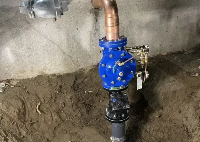 A newly installed water valve assembly with blue components is partially buried in soil near a concrete wall.