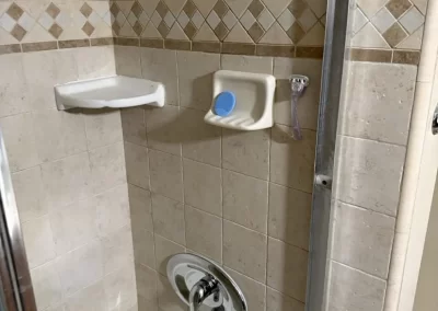 Shower with beige tiles, a missing showerhead, and a soap dish holding a blue-lidded container.
