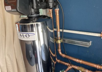 A water softener system with copper pipes installed against a blue wall near a curtain.