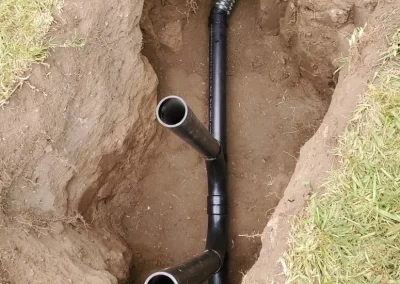 Two black pipes in a dug-up hole in the ground, surrounded by grass and soil.