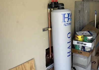 A water filtration tank is installed against a garage wall near boxes, paint cans, and a folded ladder.