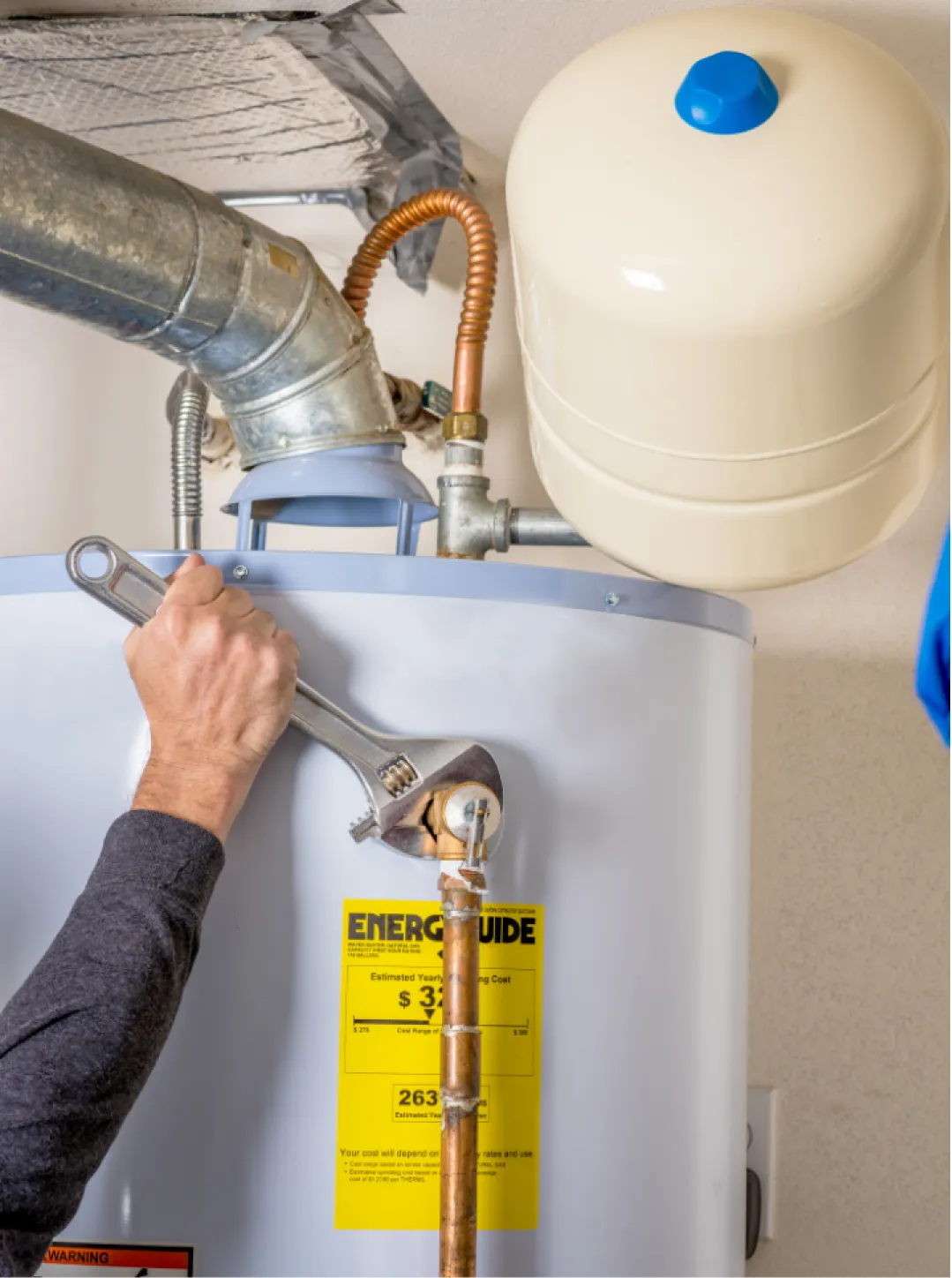Person using a wrench to tighten a pipe on a water heater with an energy guide label.