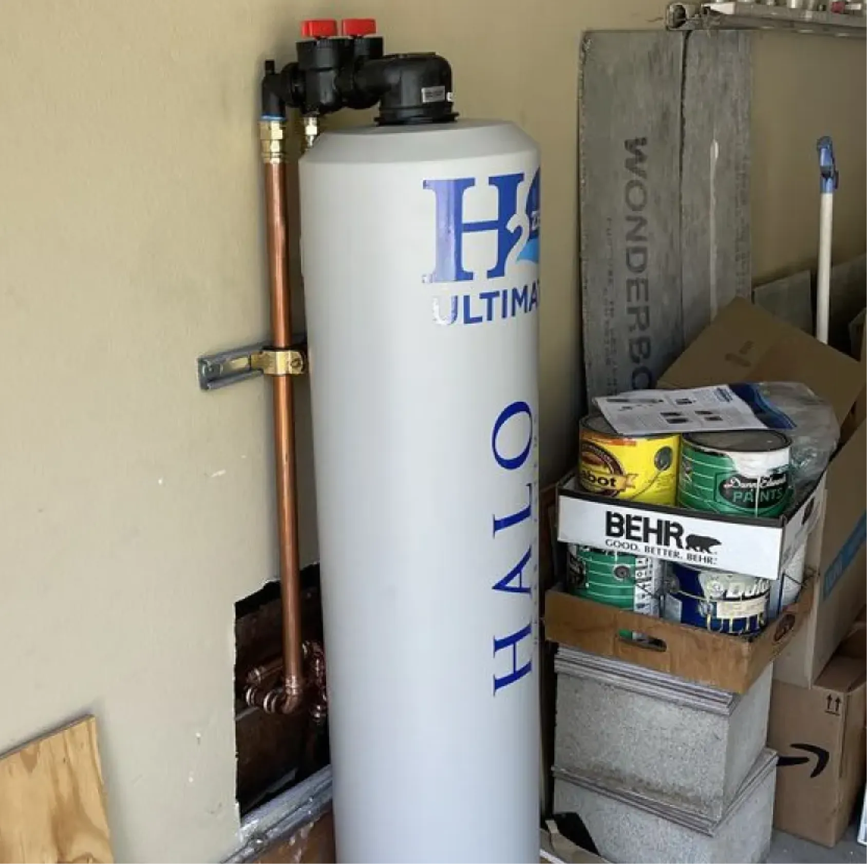 A water filtration tank labeled "HALO H2 ULTIMA" stands next to paint cans and boxes in a garage.
